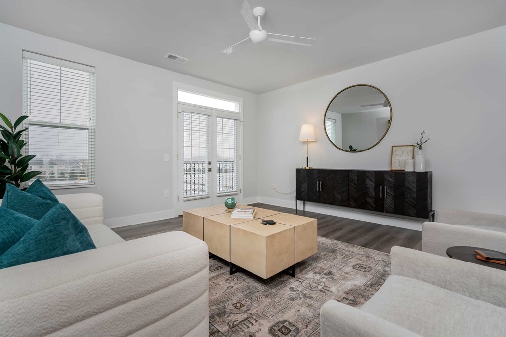A living room with a white couch, a wooden coffee table, and a round mirror on the wall.