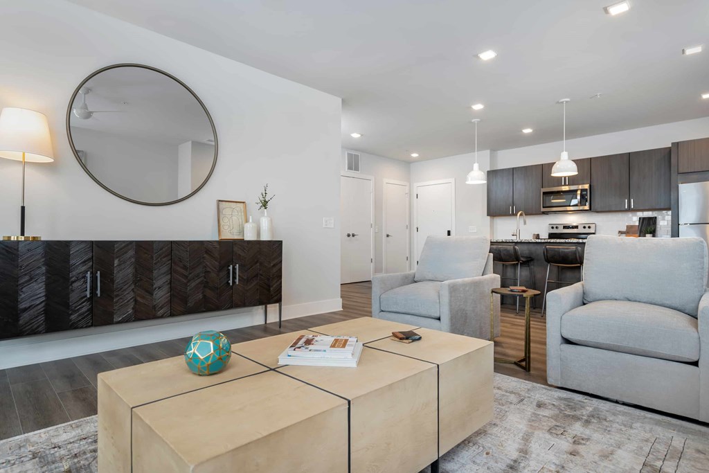A modern living room with a white wall, a round mirror, and a wooden coffee table.