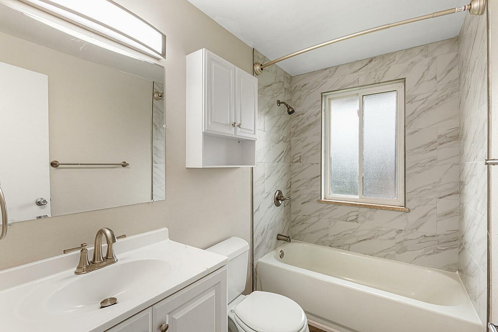 A white bathroom with a marble wall and a window.