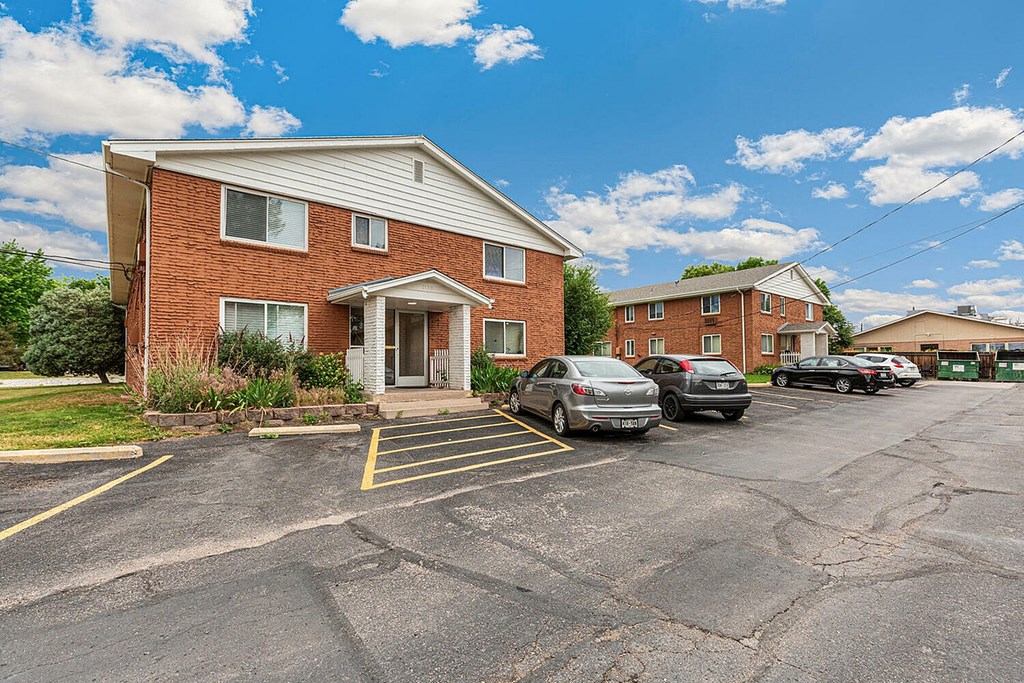A parking lot in front of a brick building with cars parked.