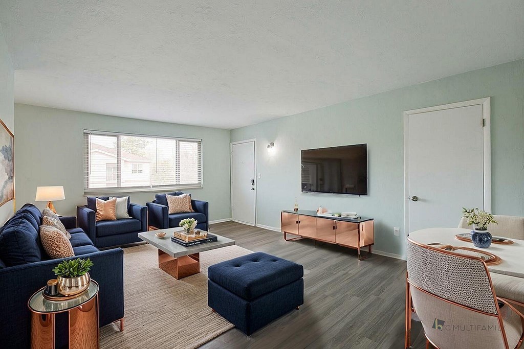 A living room with a dark blue sofa, a white table, and a TV on the wall.
