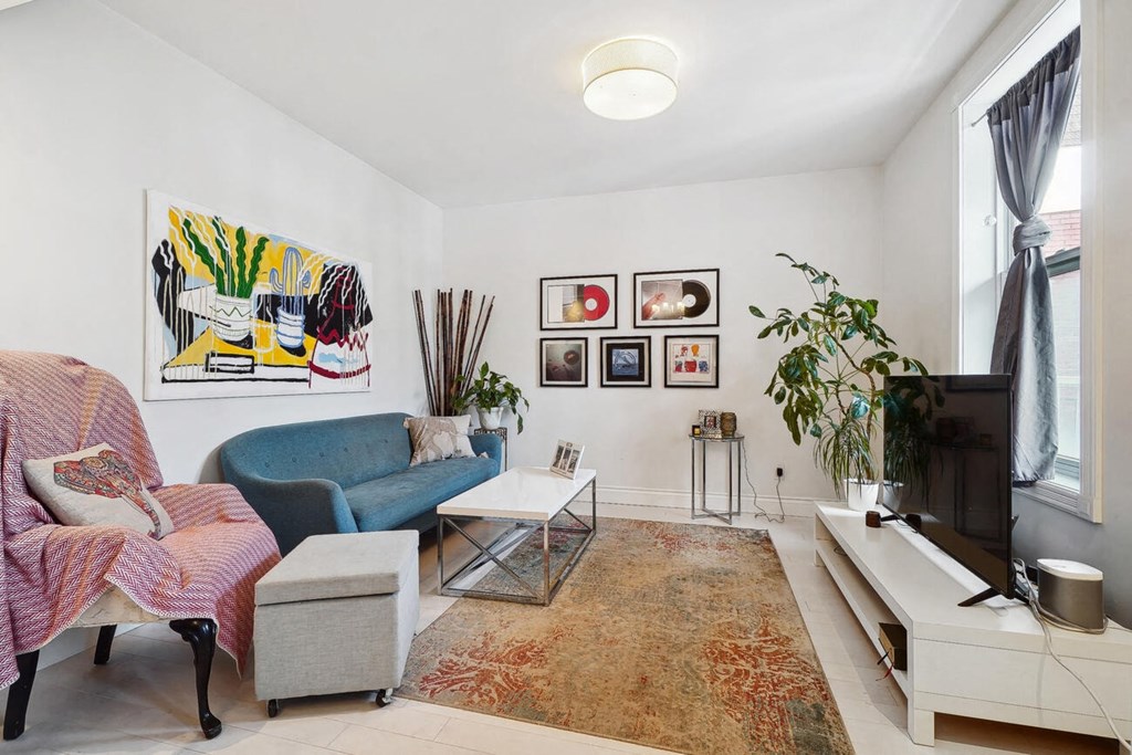 A living room with a blue couch, a pink chair, and a painting on the wall.