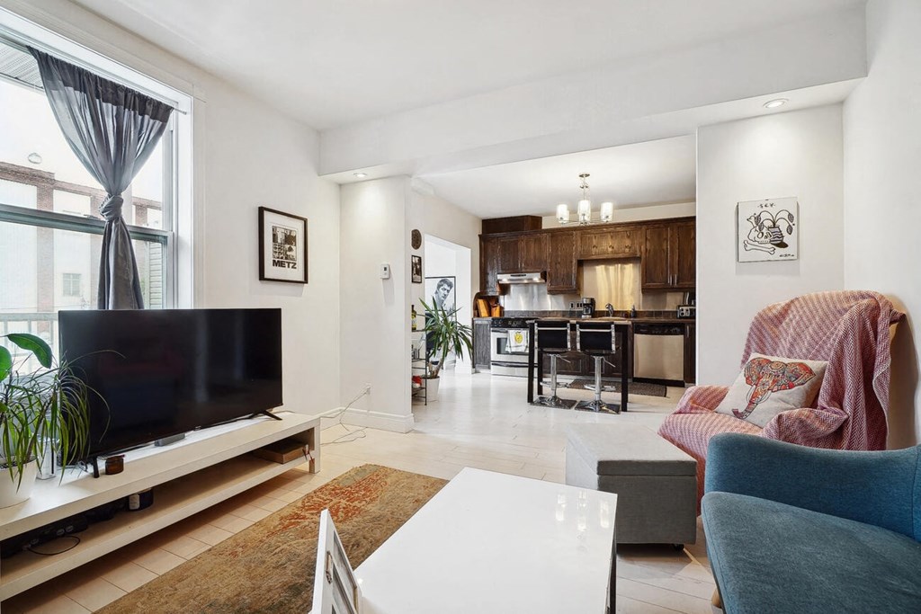 A modern living room with a flat screen TV and a kitchen in the background.