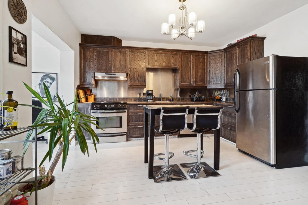 A kitchen with a black fridge and a black table with four chairs.