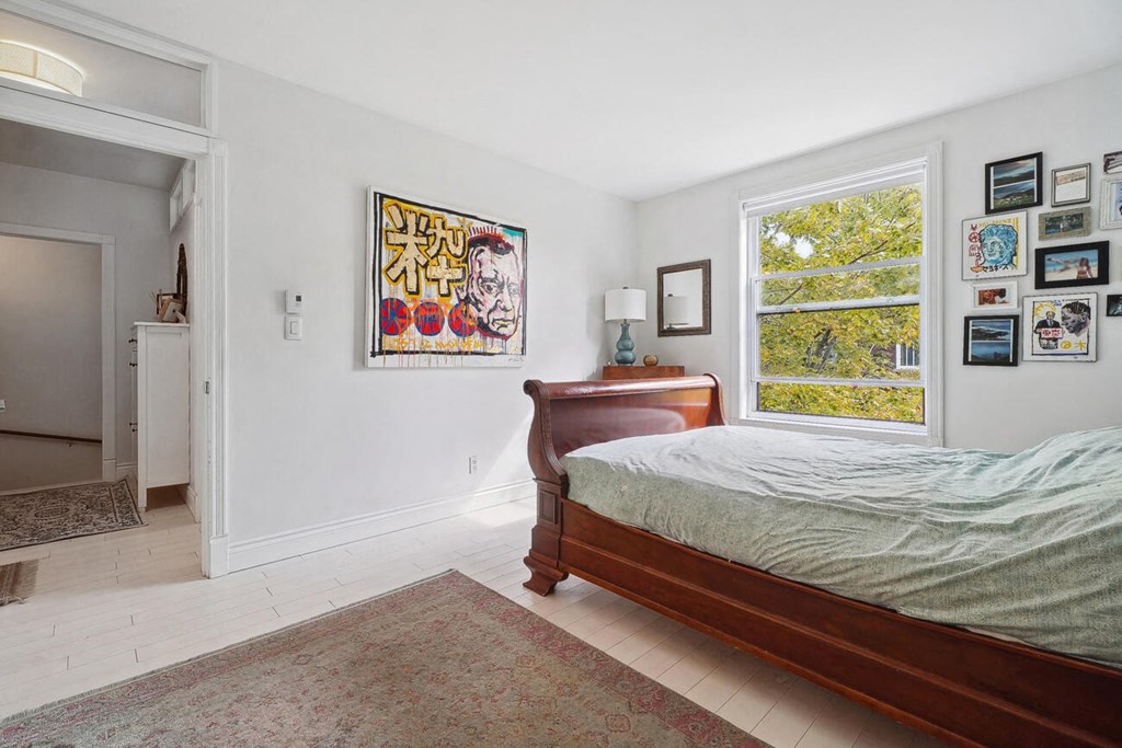 A bedroom with a bed, a rug, a painting, and a window.