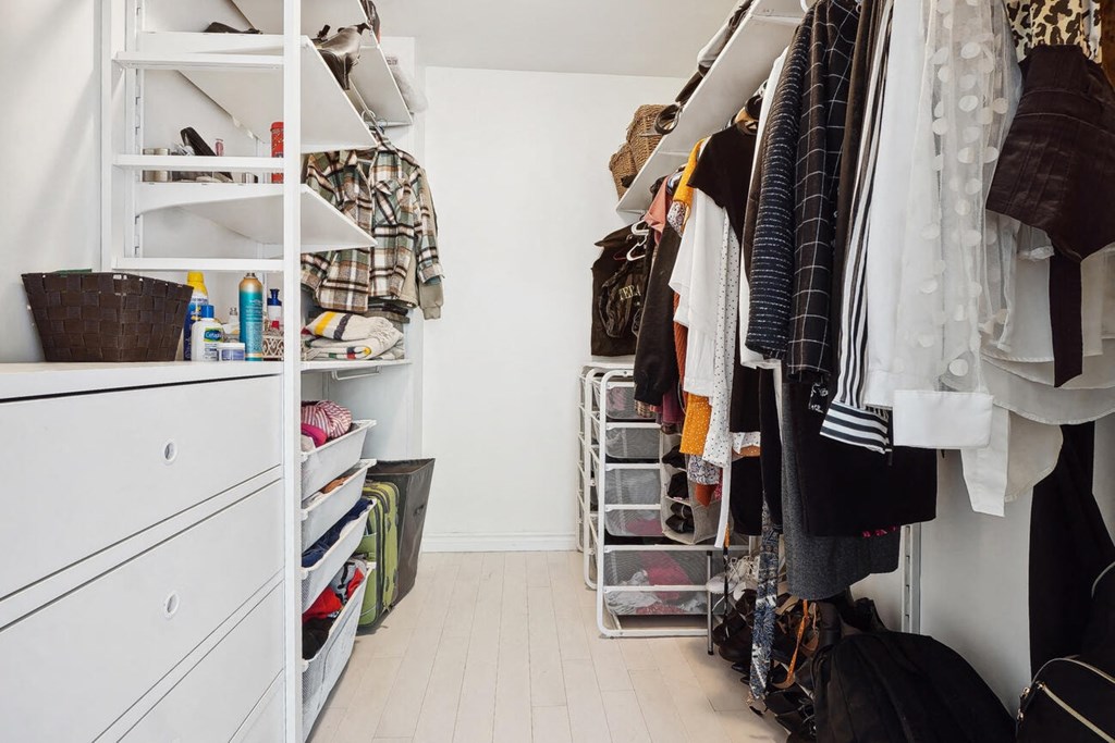 A white closet with clothes hanging and shelves with items.