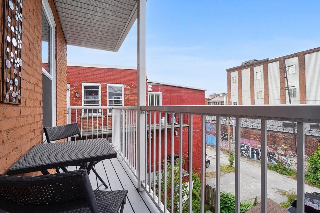 A balcony with a table and chairs overlooks a graffiti-covered area.