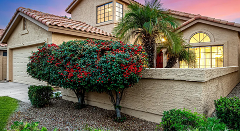 A house with a red roof and a tree with red flowers in front.