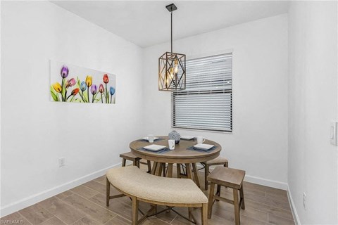 A dining room with a table set for two and a painting of flowers on the wall.