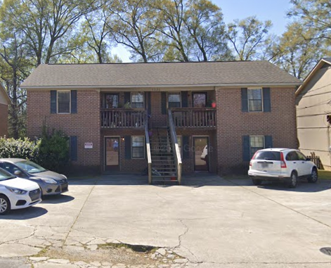A two-story brick house with a porch and a car parked in front.