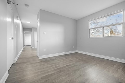 A spacious room with wood flooring and a large window.