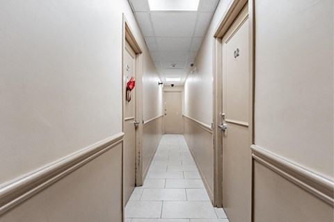 A long hallway with doors on both sides and a red fire alarm on the wall.