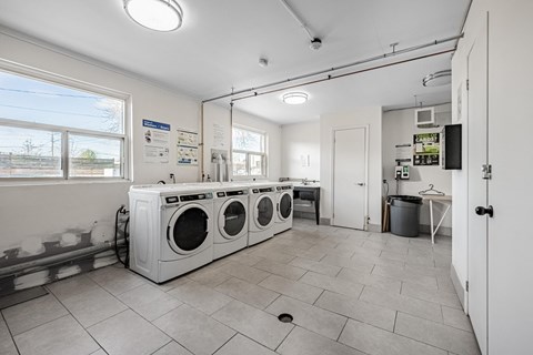 A laundry room with three washing machines and a door to another room.
