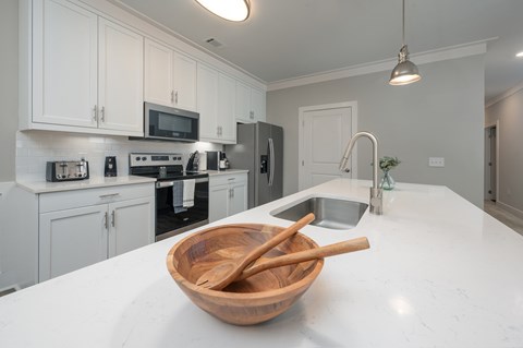A kitchen with white cabinets and a wooden bowl on the counter.