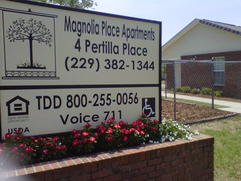 A sign for Magnolia Place Apartments is shown in front of a building.