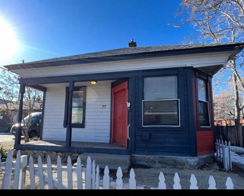 A small house with a red door and a white picket fence.