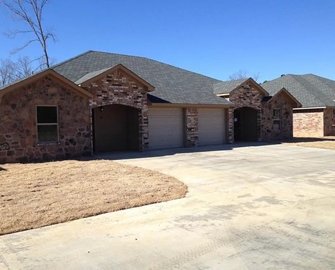 A house with a grey roof and stone exterior with a driveway in front.