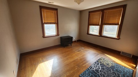 A room with wooden floors and two windows with blinds.
