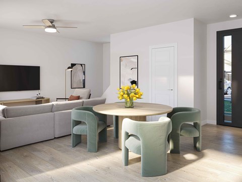 A living room with a grey couch, a round table with four chairs and a vase of yellow flowers.