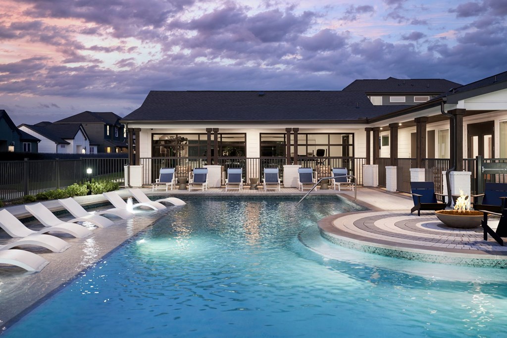 A large swimming pool in front of a house with a sunset in the background.