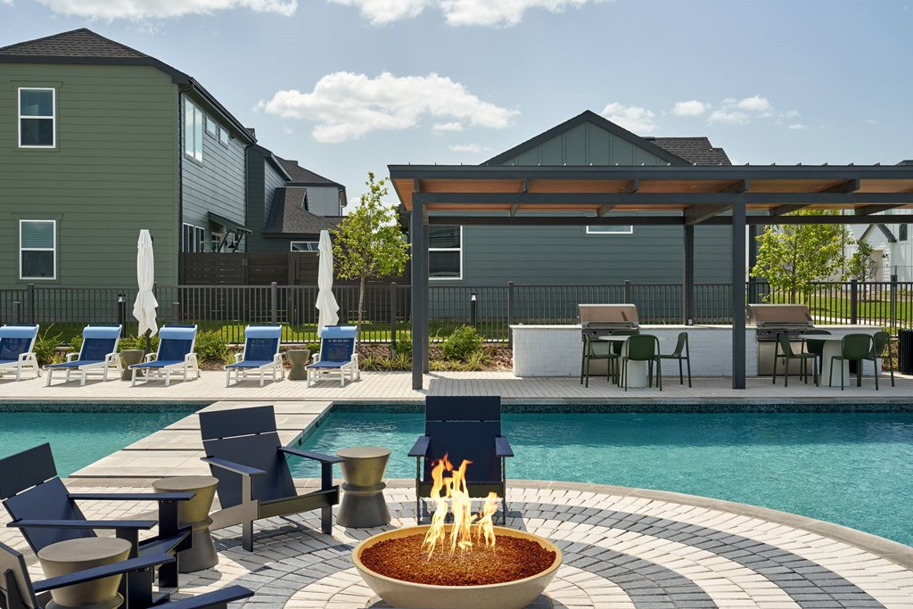 A fire pit sits in the middle of a pool surrounded by chairs and tables.