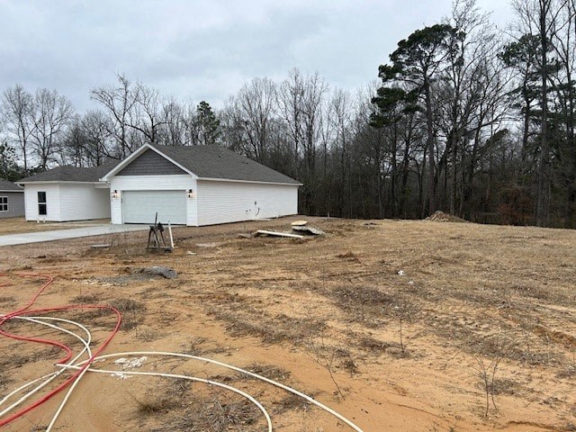 A white building with a grey roof is surrounded by bare trees and a dirt field.