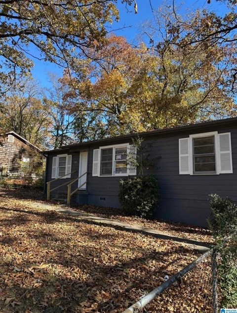 A house with a grey exterior and white windows is surrounded by trees with autumn leaves.