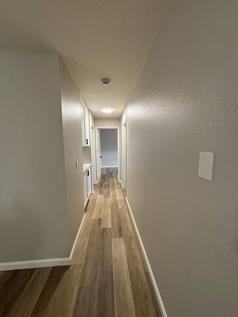 A long hallway with wood floors and white walls.