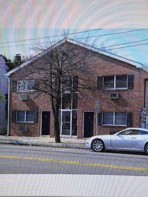 A silver car is parked on the side of a street in front of a brick building.