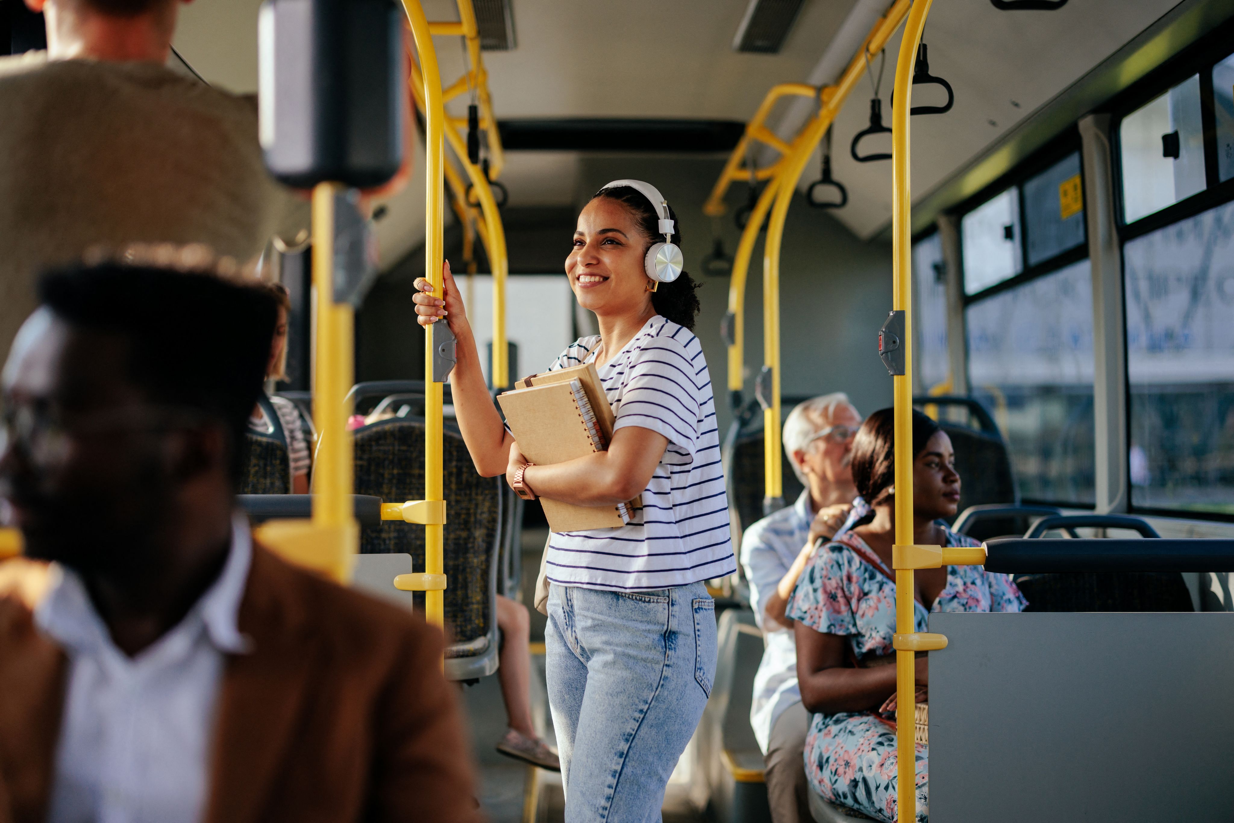 A woman in a striped shirt is holding onto a pole while riding a bus.
