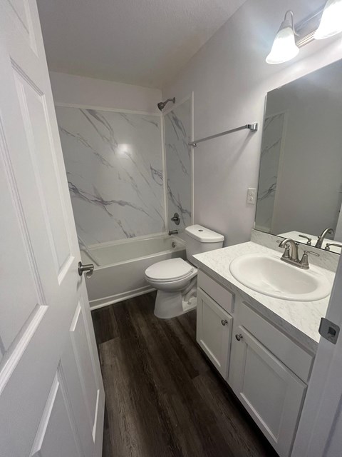 A white bathroom with a marble wall and wood flooring.