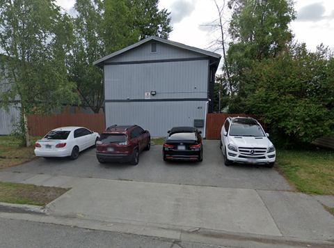 Three cars parked in front of a grey building.