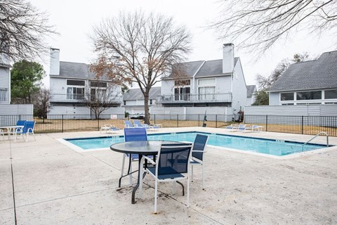 A pool with a table and chairs in front of a house.