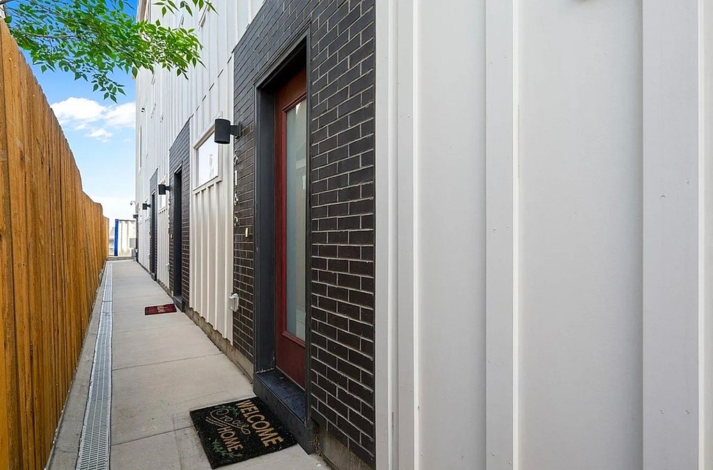 A narrow alley with a red door and a black mat on the sidewalk.