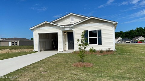 A small white house with a garage door open and a tree in front of it.