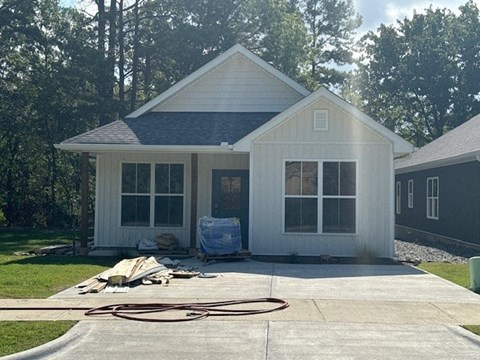 A house with a grey roof and white walls is surrounded by trees.