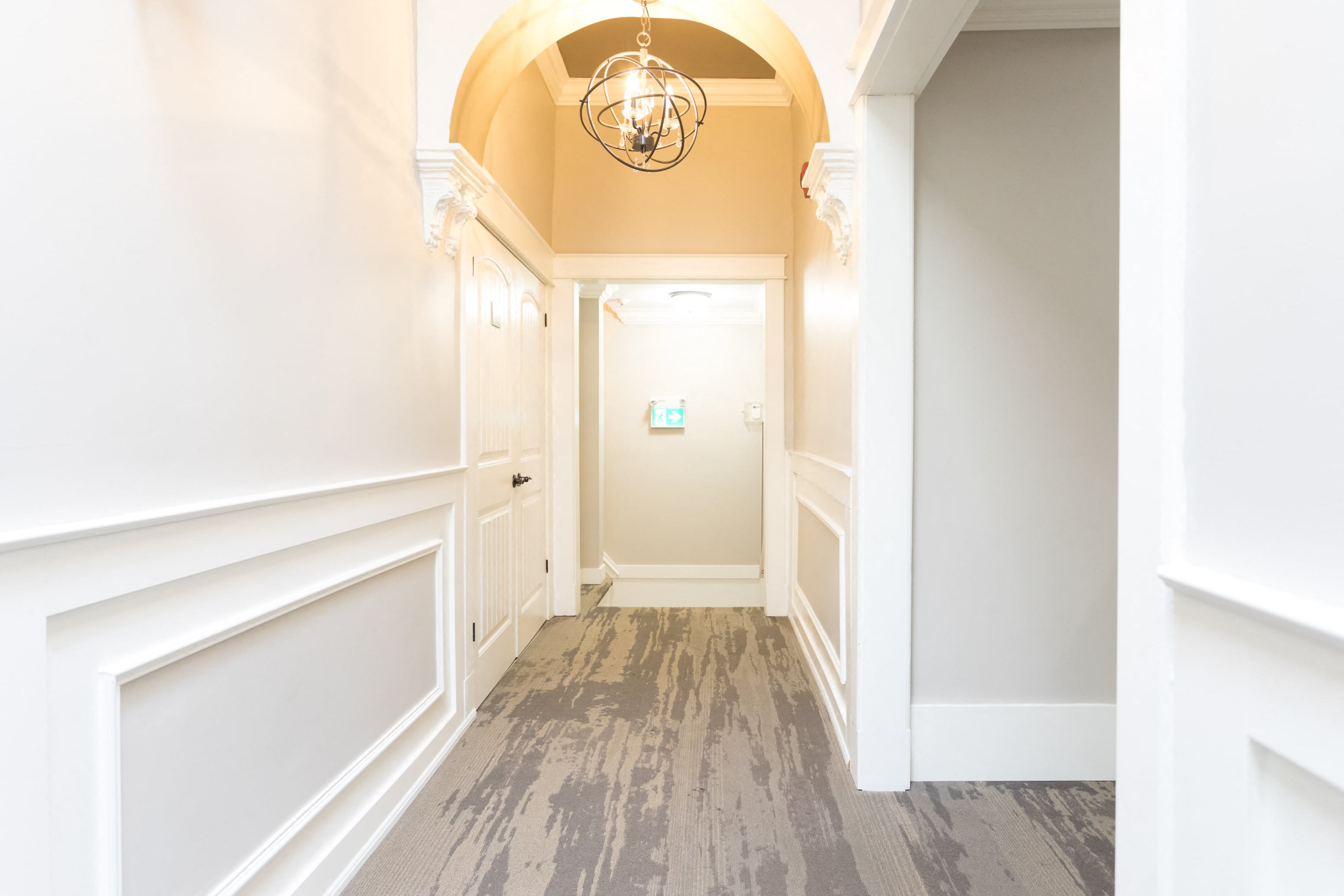 A hallway with a chandelier and a door at the end.