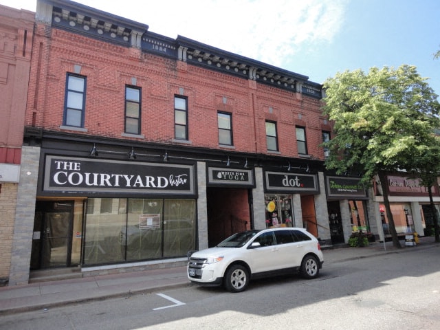 A white car is parked in front of a red building with a sign that says "The Courtyard".