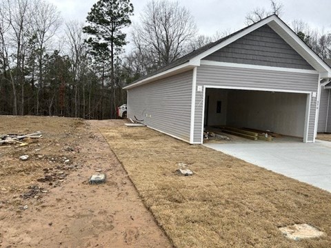 A garage with a grey roof is situated in a yard with a dirt path leading to it.