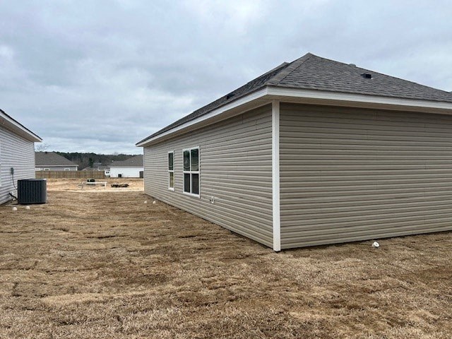 A single-story house with a grey siding and a brown roof is situated in a field.