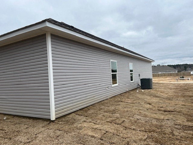 A small, single-story building with a grey siding and a white trim is situated in a dry, brown field.