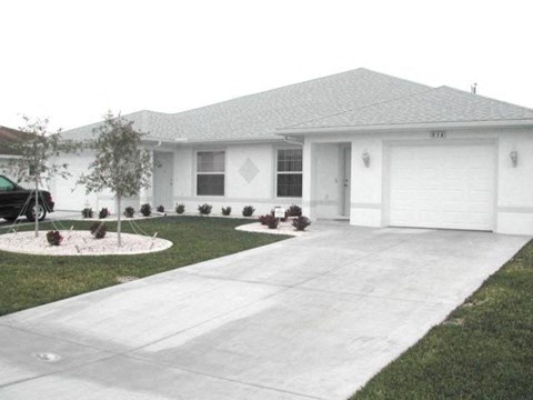 A white house with a grey roof and a grey concrete driveway.
