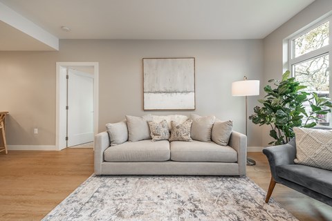 A living room with a grey couch and a large painting on the wall.