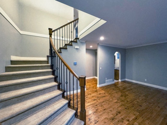 A staircase with a wooden handrail and beige carpeted steps leads up to a landing with a door and a wall-mounted light fixture.