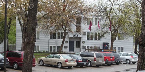 A white building with a black door and windows is surrounded by parked cars.