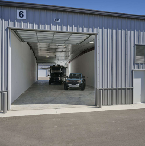 A blue building with the number 6 on it has a white truck and a black jeep parked in it.