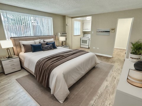 A bedroom with a large bed and a small kitchenette in the background.