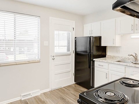 A black refrigerator in a kitchen with white cabinets and a stove.