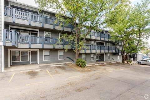 A parking lot in front of a grey apartment building.