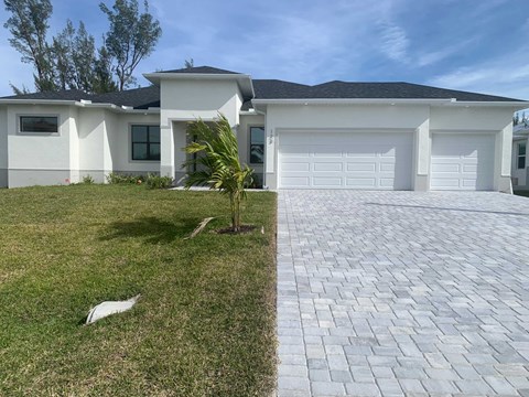 A white house with a grey roof and a brick driveway.